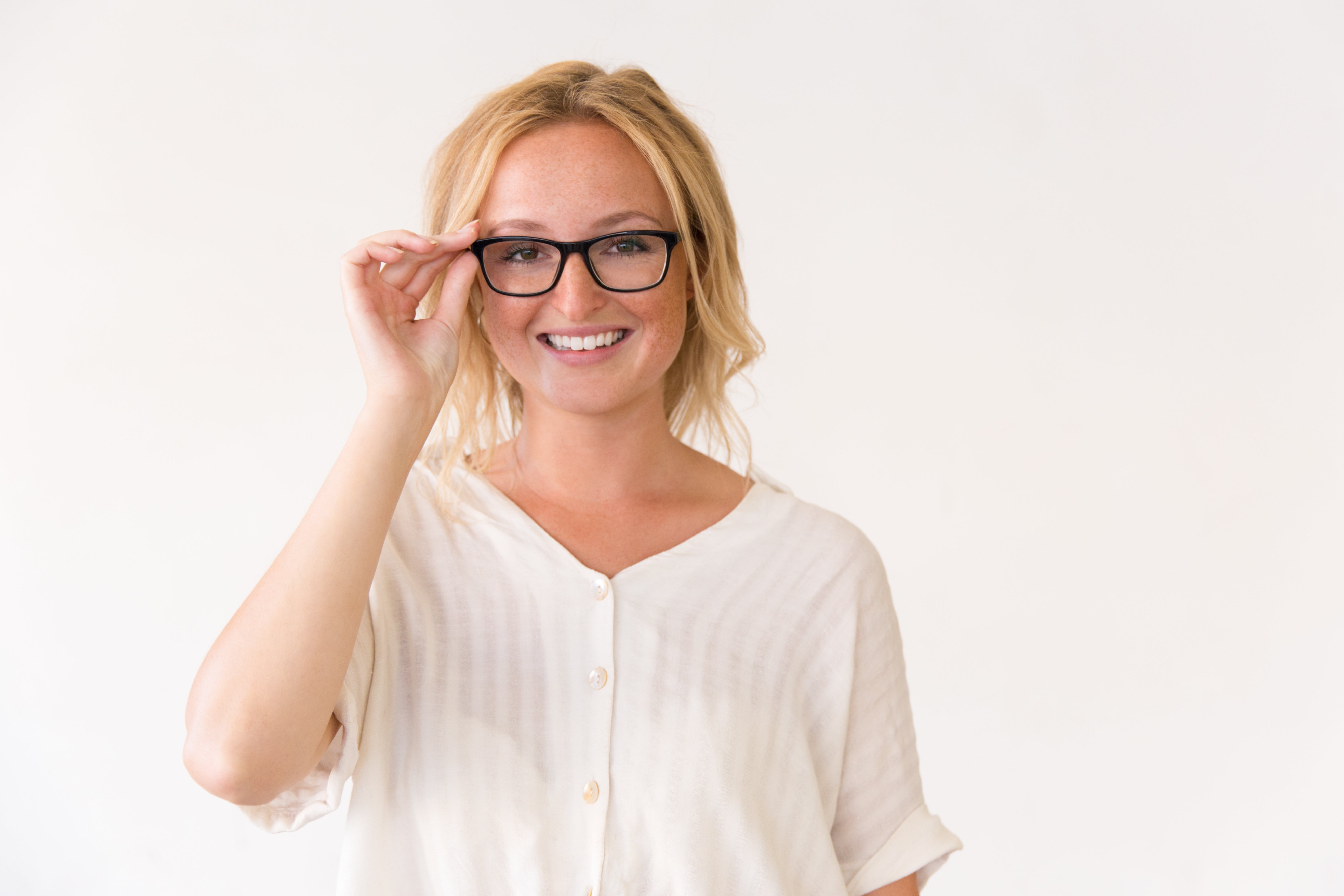 Woman wearing glasses and a white blouse against a plain background