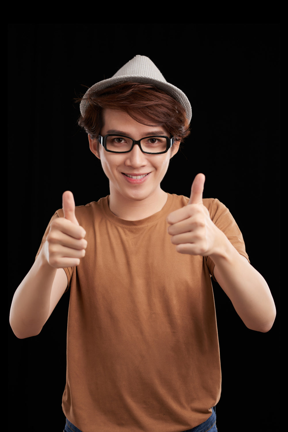 Person wearing a brown shirt and gray hat giving a thumbs-up gesture on a black background